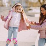 Excited young woman preventing from falling down daughter wearing protection pads while roller skating on concrete ramp during active leisure in sunny spring day