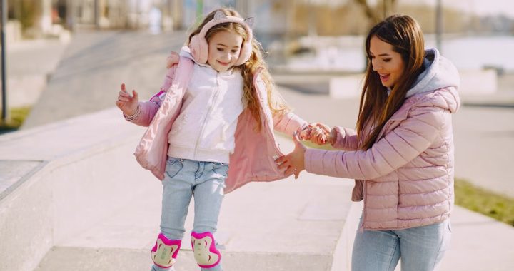 Excited young woman preventing from falling down daughter wearing protection pads while roller skating on concrete ramp during active leisure in sunny spring day